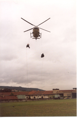 Helicóptero de Policía Nacional en vuelo de poca altura con dos miembros de Unidades Especiales en el exterior, durante el  descenso en rapel.