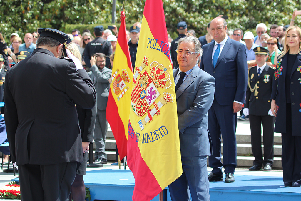 Policía Nacional en posición de saludo y cabeza inclinada ante la bandera de España que sujeta el Ministro del Interior.