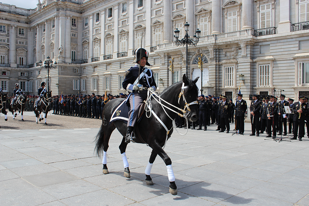 En prime plano, una policía de la Unidad de Caballería montada a caballo desfilando y al fondo una formación de Policías Nacionales.