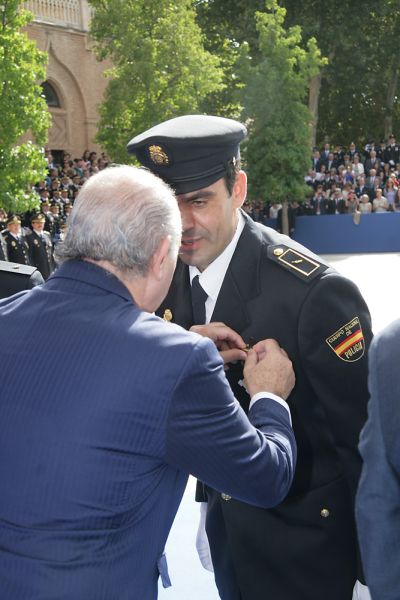 El Ministro del Interior imponiendo una condecoración a un Policía Nacional con uniforme de gala en la mesa de entrega de condecoraciones.