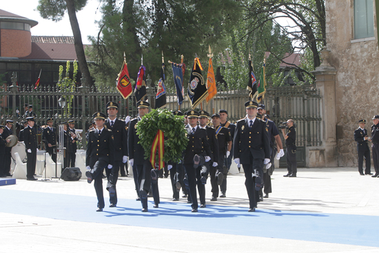 Una formación de Policías Nacionales rindiendo honores a los caídos, portando banderines de distintas unidades policiales y una corona.