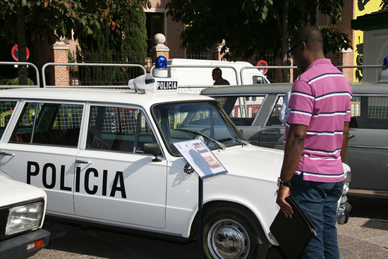 Un visitante de la exposición abierta observando un vehículo antiguo de la Policía, modelo Seat 124D de color blanco.
