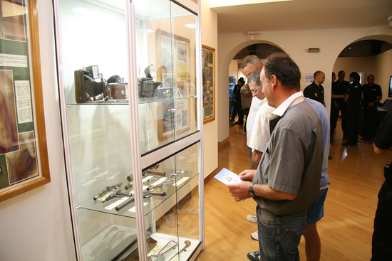 Varios visitantes observan varias armas y cámaras fotográficas antiguas en el interior de una vitrina de la exposición.