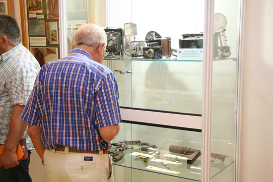 Un visitante observa varias armas y cámaras fotográficas antiguas en el interior de una vitrina de la exposición.