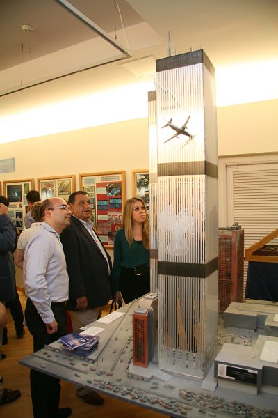 Varios visitantes observan una maqueta de un las torres gemelas y un avión a punto de estrellarse contra ellas. 