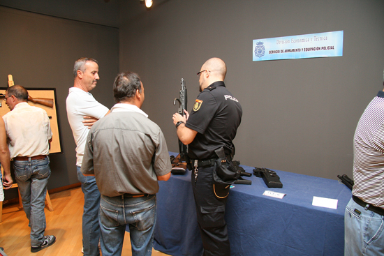 Un Policía Nacional con un subfusil en las manos dando una explicación sobre la misma a unos visitantes.
