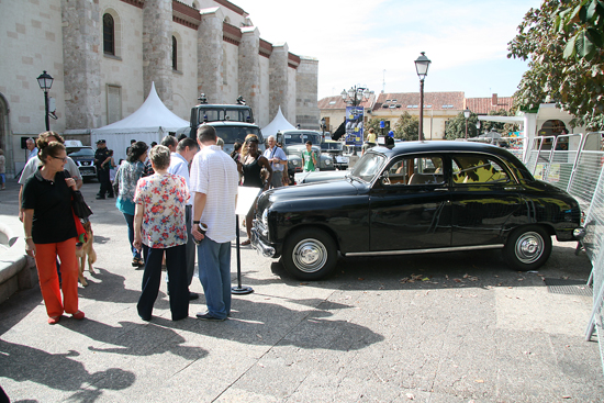 Varios visitantes de la exposición abierta observando un vehículo antiguo de la Policía, modelo Seat 1400 de color negro.