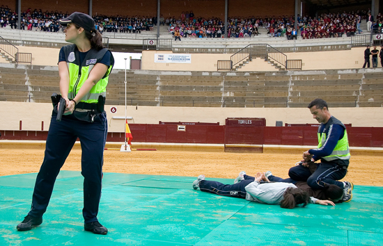 Exhibición. Un policía engrilleta a dos personas tumbadas en el suelo, mientras una policía da protección con su arma.