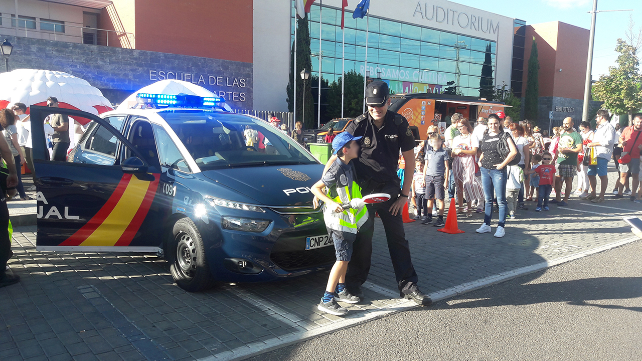 Agente de policía delante un de un vehículo policial con un niño que lleva chaleco reflectante y una señal de stop