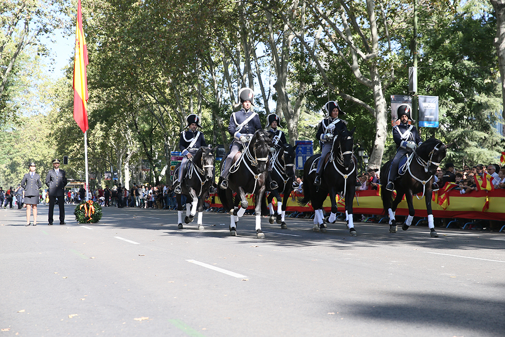 Desfile de la Unidad Especial de Caballería de la Policía Nacional, en una formación en linea de tres, vistiendo traje de gala de época.