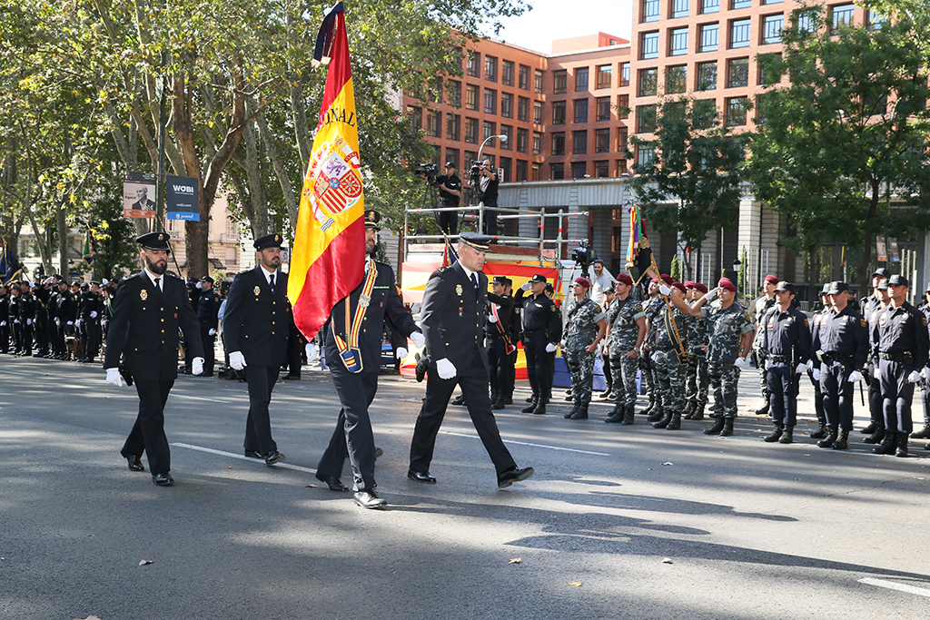 Un Policía Nacional porta la bandera de España, escoltado por otros tres policías