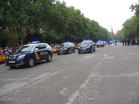 Desfile de vehículos de la Policía Nacional, al paso vehículos tipo zeta en formación de cuña, con las luces de emergencia encendidas.