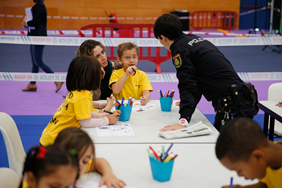 Mesa con varios niños coloreando dibujos policiales y una agente de policía ayudándoles.