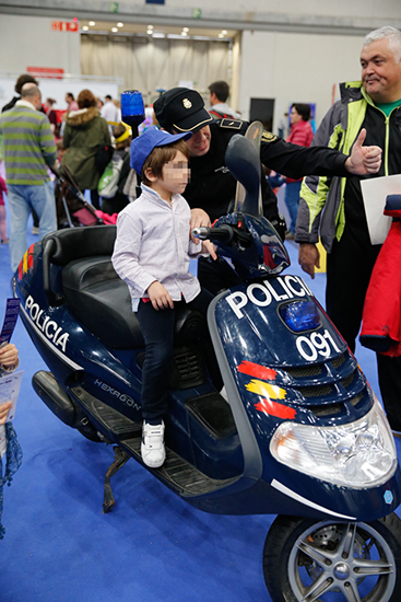 Niño posando con un agente de policía. El niño está subido en una motocicleta y lleva una gorra de policía.