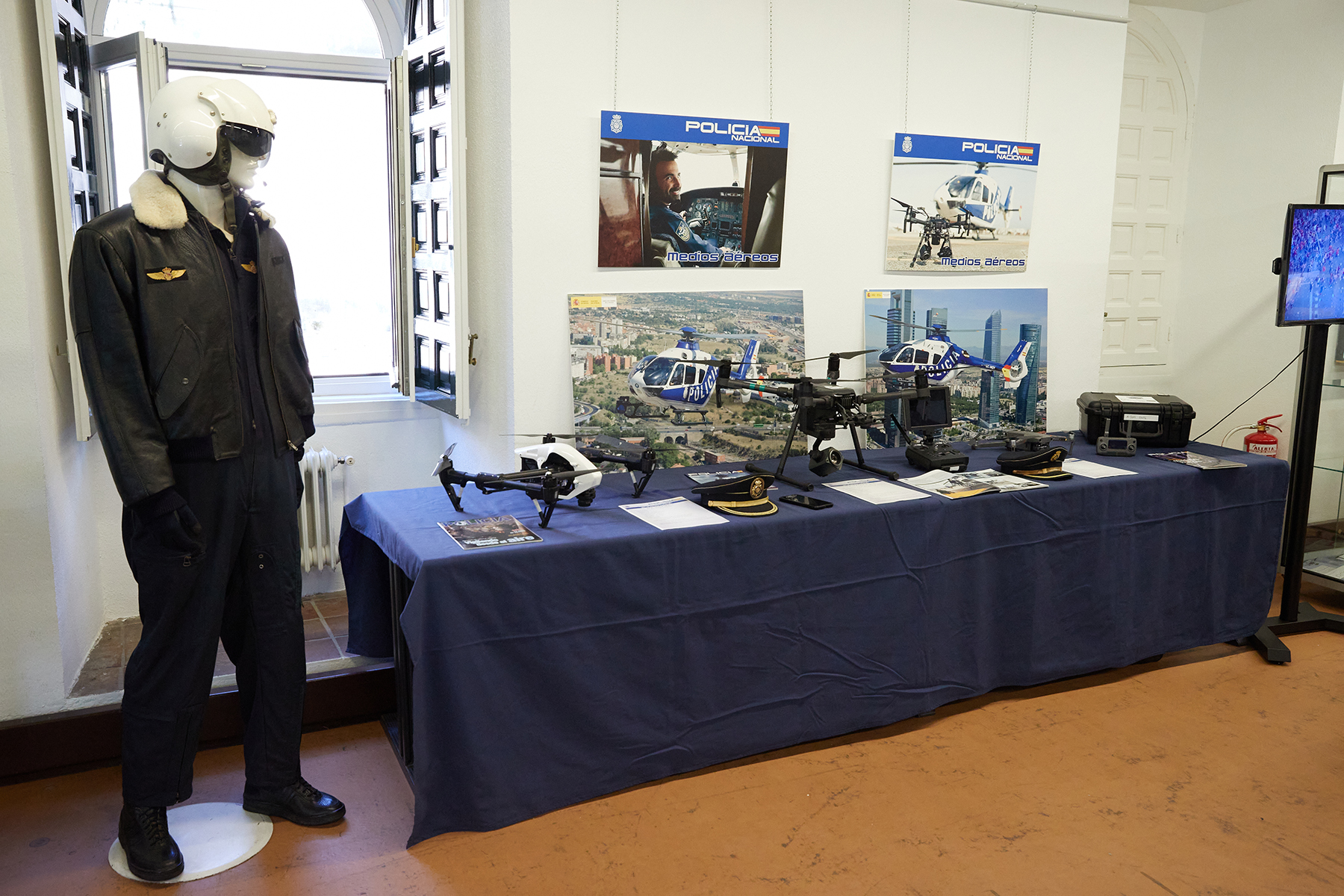 Mesa en la cual se exponen diversos drones utilizados por la Policía Nacional, junto a un maniquí que lleva un traje de los Médios Aéreos.