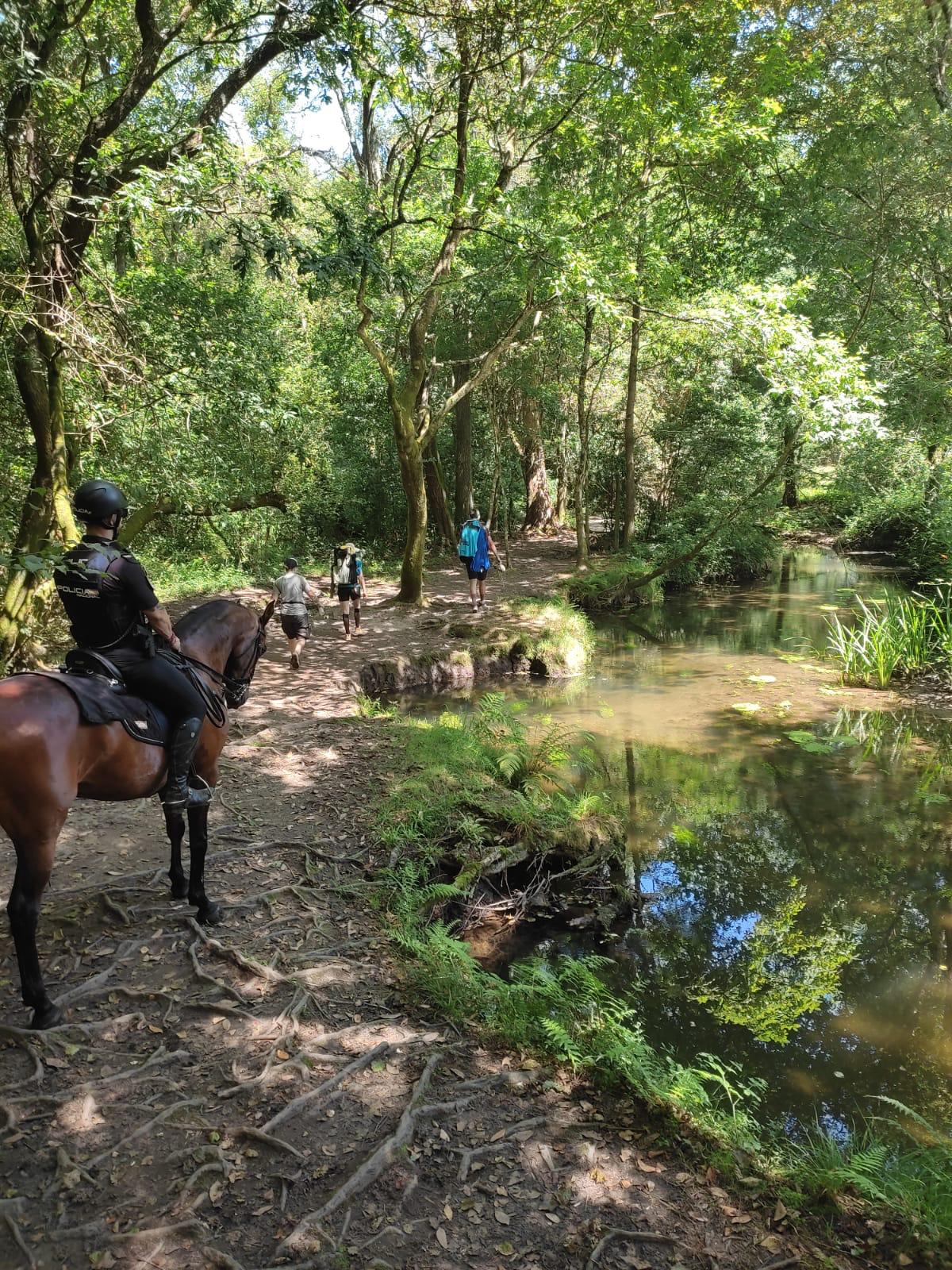 Un Policía montado a caballo en un camino con vegetación y un río detrás de tres peregrinos