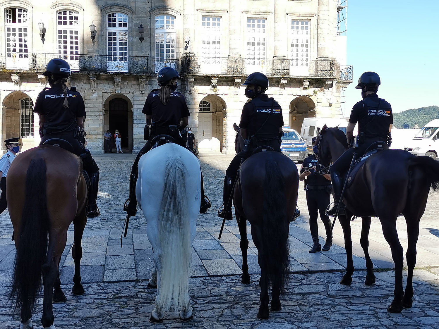 Cuatro Policías de la Unidad de Caballería montados en sus caballos, visto de espaldas, en la Plaza del Obradoiro
