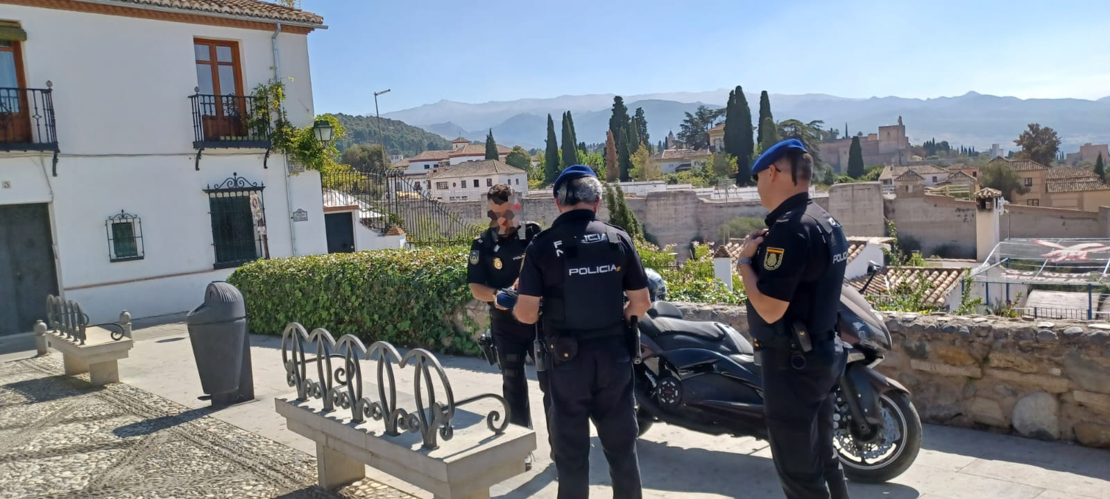 Tres agentes de la Policía Nacional, junto a una moto oficial,  en un lugar elevado de la ciudad.