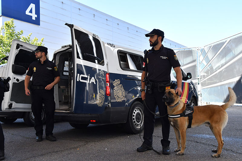 Dos  agentes de la Unidad de Guías Caninos  uno con perro,  junto al vehículo de transporte para el perro.