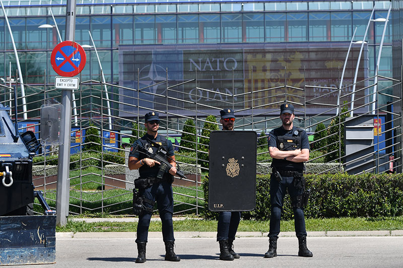 Tres agentes de la Policía Nacional, uno portando escudo policial, delante de la entrada al recinto de la cumbre.
