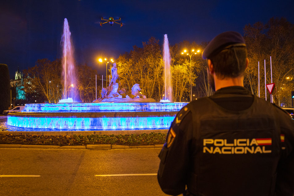 Agente de la Policía Nacional de espaldas frente a la fuente de Cibeles  iluminada en conmemoración al bicentenario de la Policía Española.