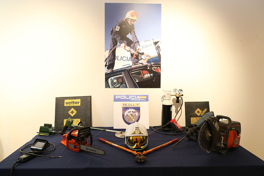 Mesa con herramientas que utiliza la especialidad GOIT, cizalla, moto sierra, etc. En la pared, cartel de mujer policía utilizando una de ellas.