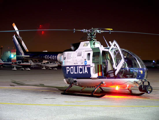 Helicóptero de la Policía Nacional, modelo BO-105, de noche,  estacionado en pista con las luces encendidas.