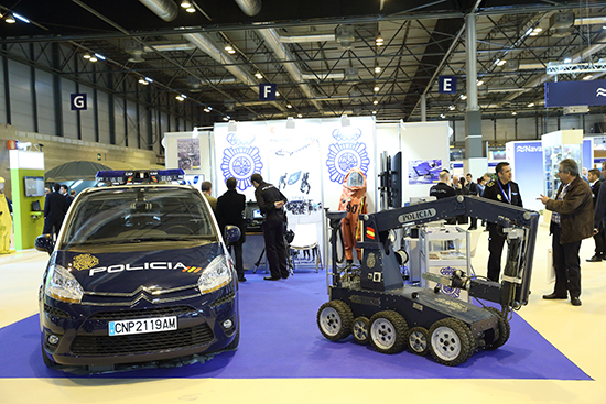 Vehículo policial y robot AUNAV,  detrás de ellos mostrador con equipos para identificación de personas y traje del TEDAX-NRBQ.