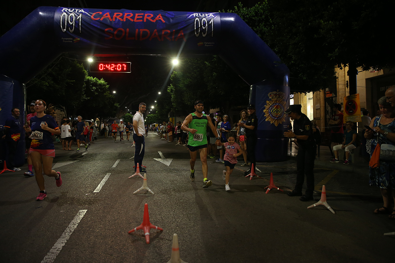 Llegada a meta de la carrera nocturna donde se ve a un hombre y una niña cogidos de la mano, corriendo, siendo aplaudidos por un hombre uniformado.