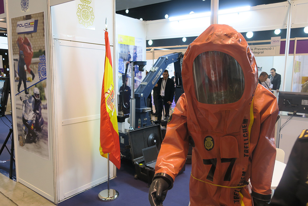 Traje de color naranja para desactivar explosivos. Detrás,  la bandera de España y el robot que se usa para la desactivación.