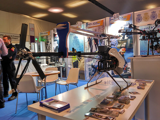 En el frontal mostrador con dron tipo helicóptero y folletos explicativos. En lateral se observa otro dron de diferentes características al anterior.